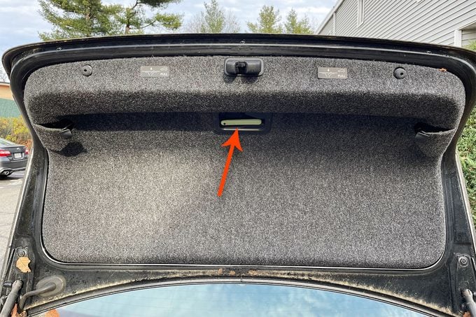 open trunk with a red arrow overlay pointing to the emergency trunk release latch
