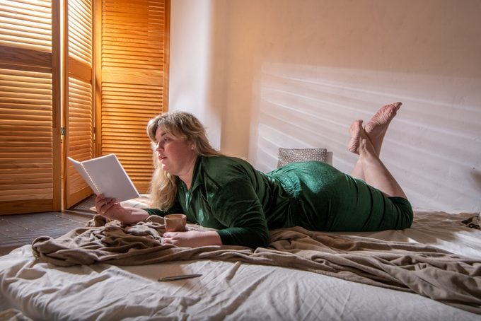 A woman reads a book while laying on a bed